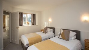 A hotel room with two beds, a window with curtains, a bedside table, and a nightstand. - Yew Tree Cottage (Ambleside)