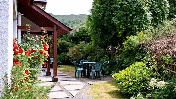 A garden with a stone pathway leading to a wooden pergola with chairs. - Yew Tree Cottage (Ambleside)