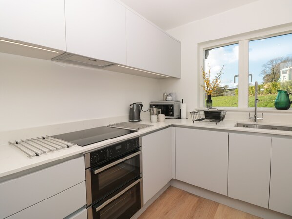 A modern kitchen with white cabinets, a stainless steel range hood, a built-in oven, a stovetop, and a window with a view of the outdoors.