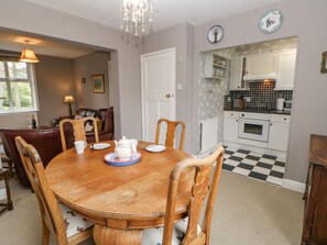 A dining room with a wooden table and chairs, a chandelier, and a view into the kitchen with a checkered floor.
