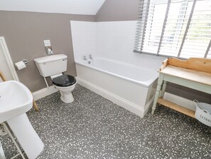 A bathroom with a white toilet, a white sink, a bathtub, and a window with blinds.