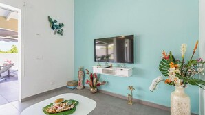 En moderne stue med en teal farvet væg, et fladskærms-tv, et hvidt konsolbord, dekorative planter og et spiseområde med en grøn måtte.