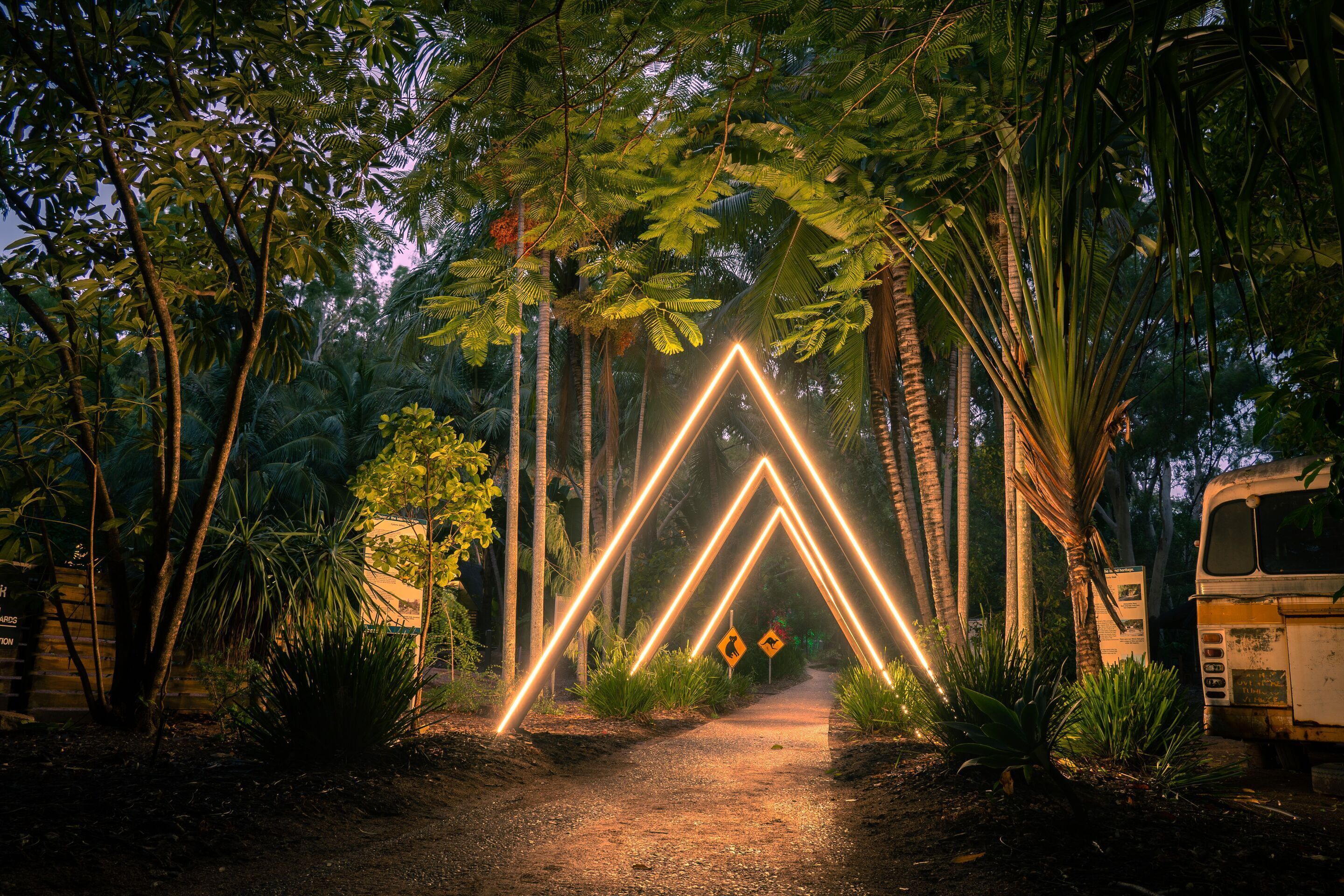 Un sendero bordeado de árboles e iluminado por luces de neón que forman un diseño geométrico.