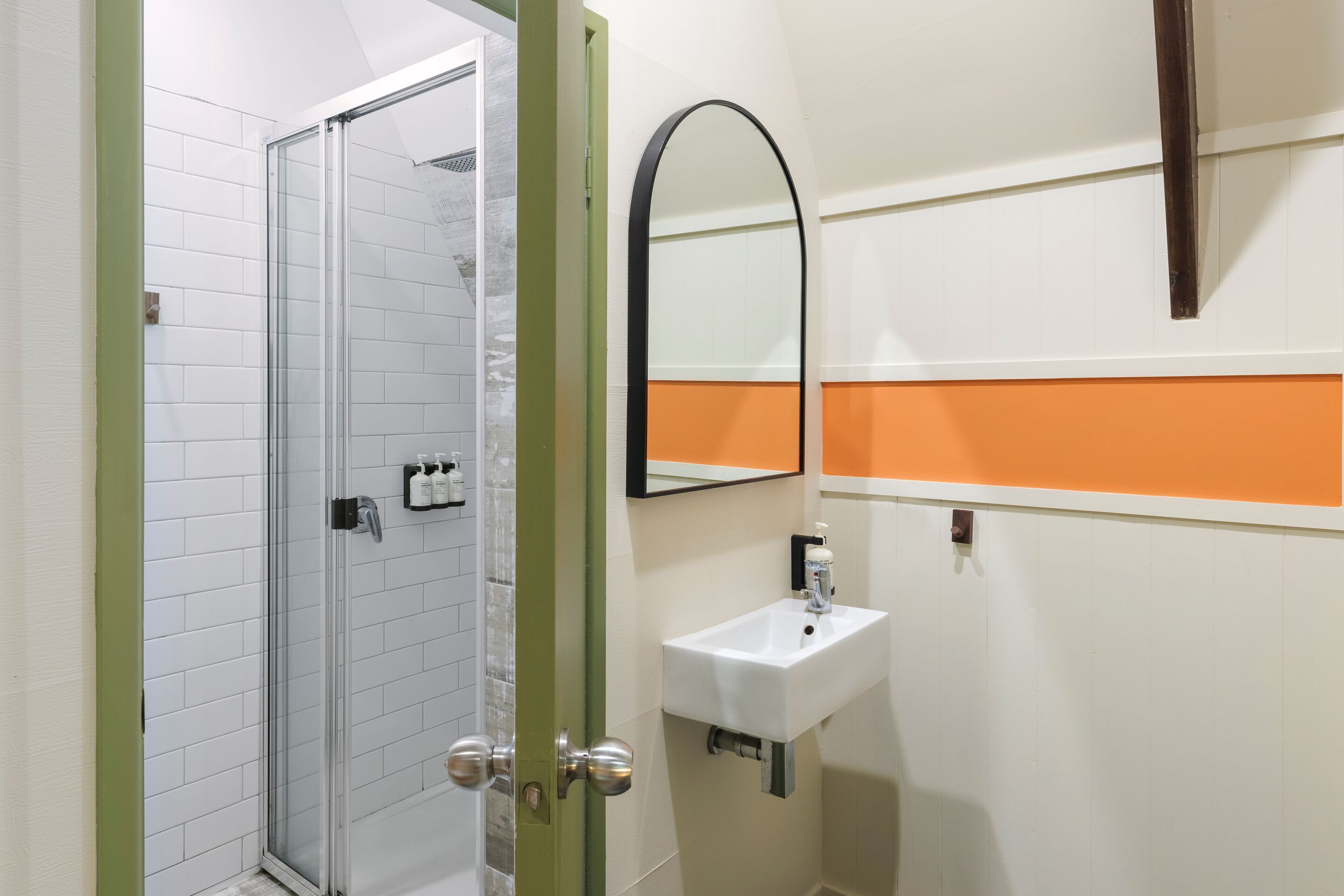 Un bany amb mampara de vidre, un lavabo blanc i un mirall.