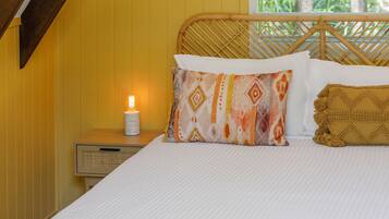 A bed with a white sheet, a wooden headboard, and two pillows. There is a nightstand with a lamp and a small radio.