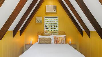 A room with a sloped ceiling, a bed with white bedding, two bedside tables with lamps, and a window with blinds.