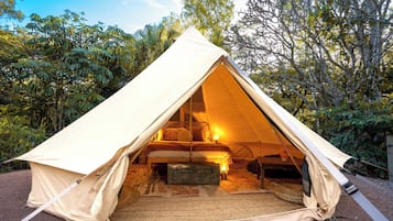 A dome-shaped tent with a bed inside, surrounded by trees.