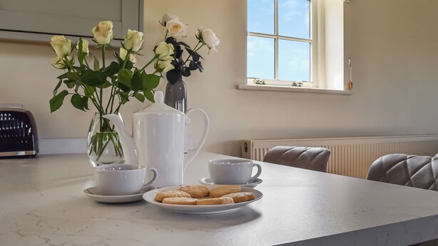Un piano di lavoro in cucina con un vaso bianco, teiera, tazze e un piatto di biscotti.