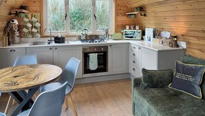 A cozy kitchen with a dining area, wooden walls, and a view of greenery outside. - Lakeview Lodge- UK40692 (Crowhurst)