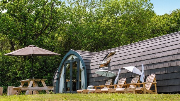 A building with a sloped roof, a covered entrance, and outdoor seating with umbrellas. - Lakeview Lodge- UK40692 (Crowhurst)