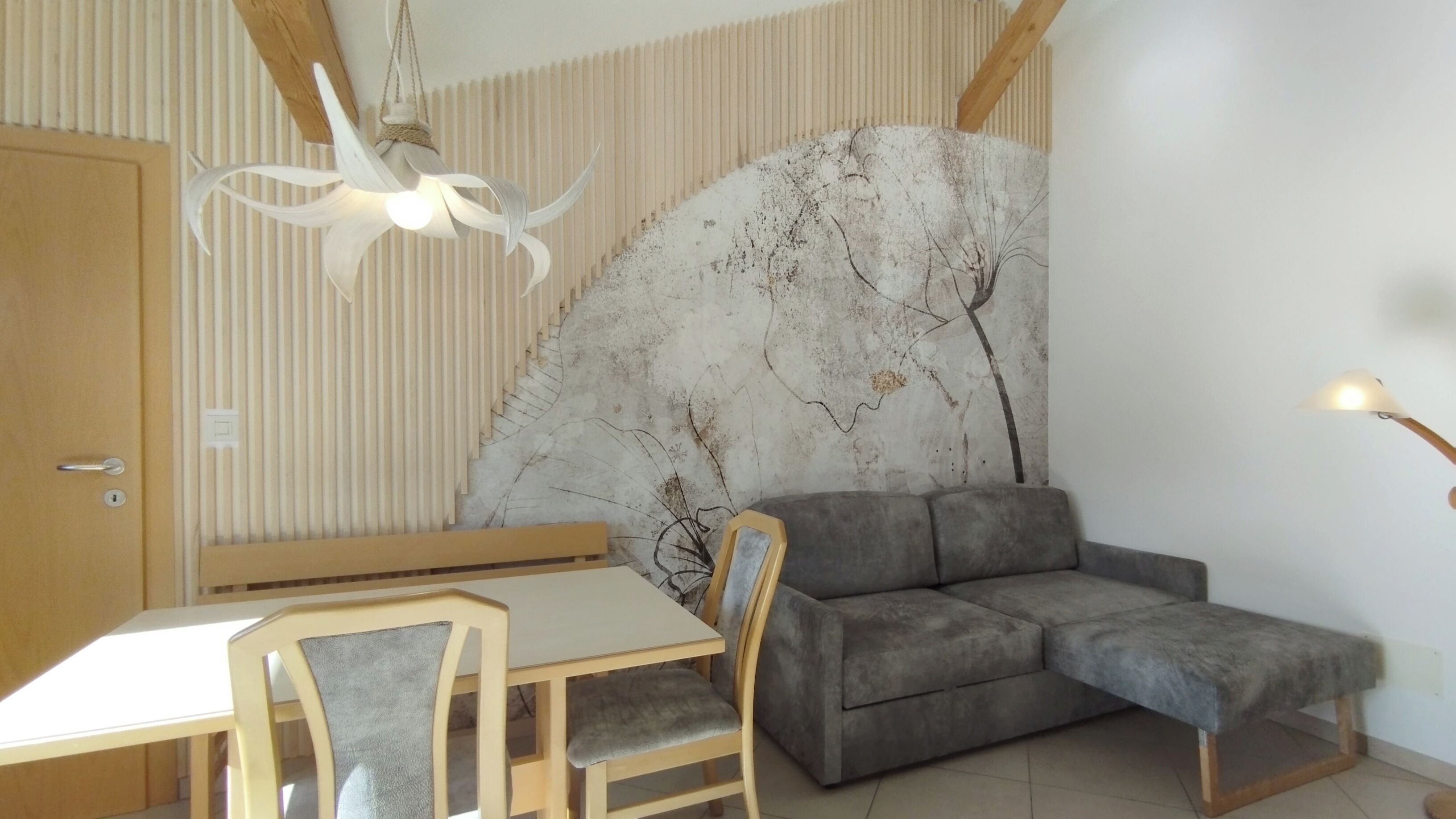 A room with a dining table, chairs, a sofa, a wall-mounted fan, and a ceiling light fixture.