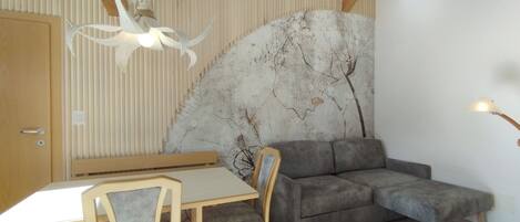 A room with a dining table, chairs, a sofa, a wall-mounted fan, and a ceiling light fixture.