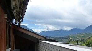 Un balcon avec une table et des chaises, donnant sur un paysage montagneux avec un village en contrebas.