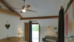 Une chambre avec un lit, un ventilateur de plafond, une chaise et une vue sur l’extérieur.