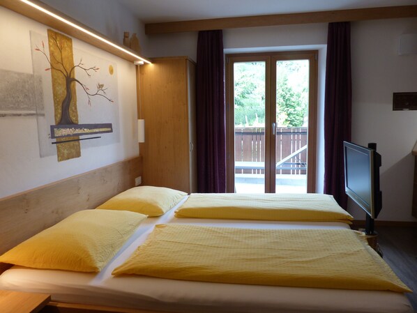 A hotel room with two beds, a TV, and a view of a balcony with a wooden railing. - Mini apartment - for 2 pers. - large balcony (Trentino-Alto Adige)