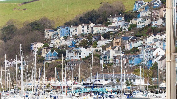 Une ville côtière avec des maisons aux couleurs vives, situées sur une colline, un port de plaisance rempli de bateaux et un lampadaire imposant.
