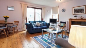 Un salon avec un canapé bleu, une table basse en verre, un téléviseur et une cheminée.