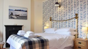 A neatly made bed with white linens and a plaid blanket, a bedside table with a lamp, and a patterned wallpaper. - 3 bedroom accommodation in Keswick (Keswick)