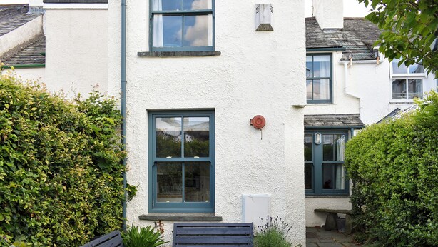 A white building with a window, a door, and a small garden area with a bench and plants. - 3 bedroom accommodation in Keswick (Keswick)
