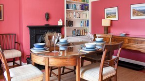 A dining area with a wooden table set for six, surrounded by chairs, a bookshelf, and a fireplace. - 3 bedroom accommodation in Keswick (Keswick)