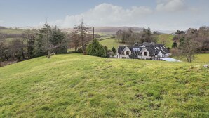 Uma casa de campo com telhado inclinado, rodeada por um monte gramado e árvores.