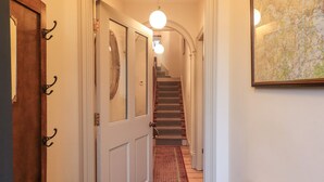 Un pasillo con una puerta de madera, una puerta blanca con paneles de vidrio, un tapete rojo con estampado, una escalera con barandilla y un mapa en la pared.