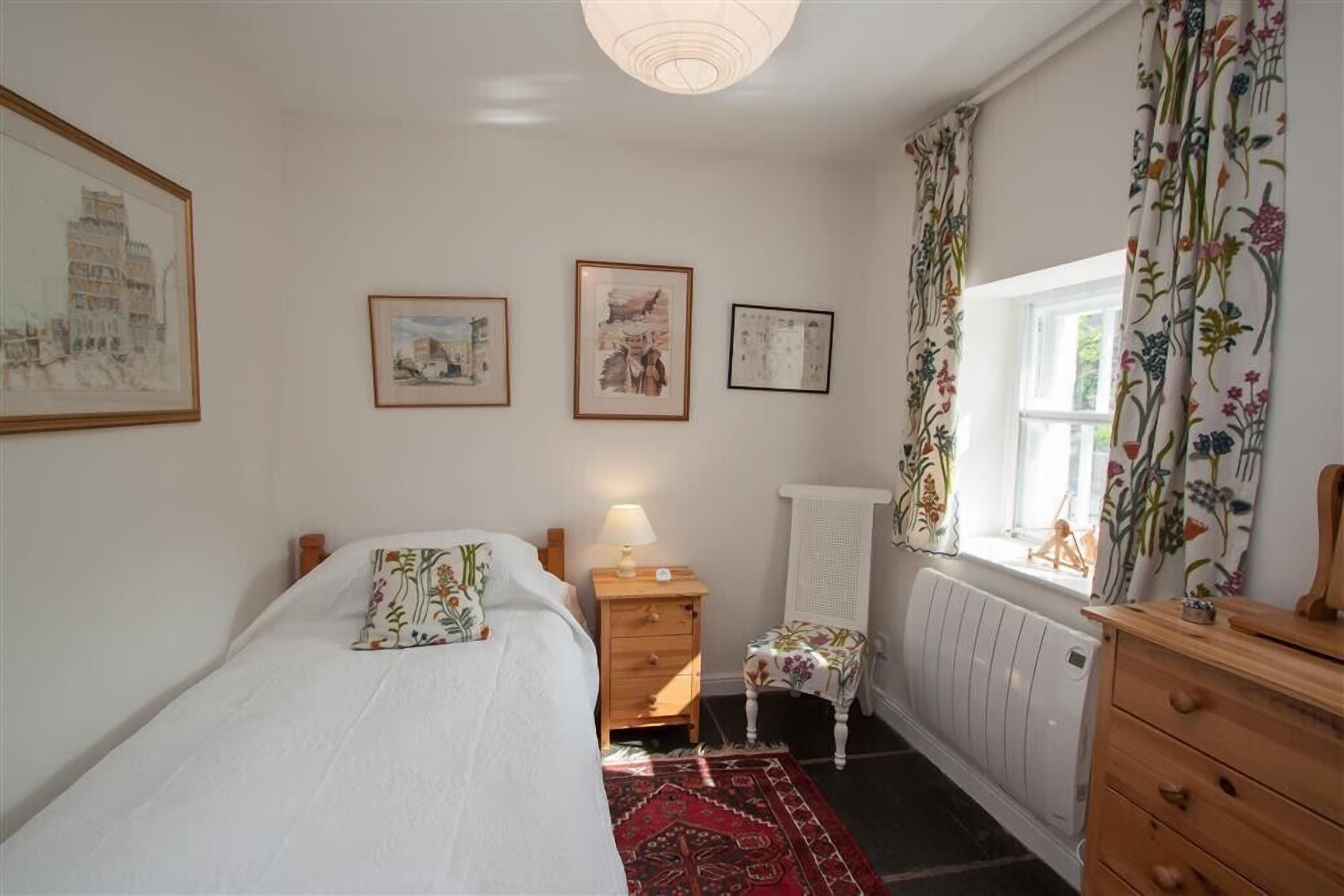 A bedroom with a bed, a nightstand, a radiator, and a window with curtains.