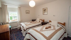 A hotel room with two beds, a desk, a chair, a window with curtains, and a hanging light fixture. - The Old Farm (Ambleside)