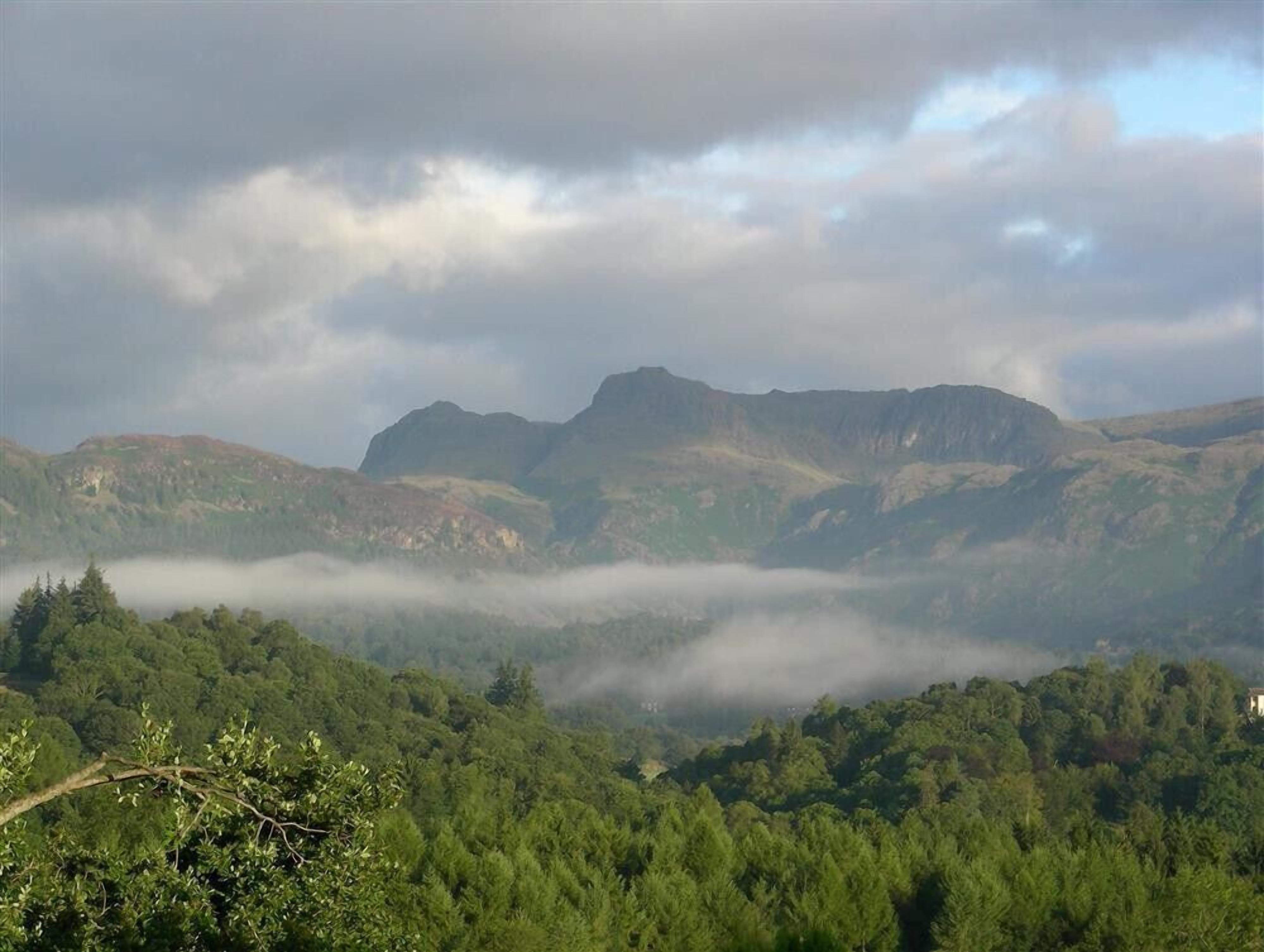 Paisagem montanhosa com floresta densa e picos cobertos de névoa.