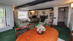 A cozy living room with a wooden dining table, green carpet, and a fireplace. - The Old Farm (Ambleside)