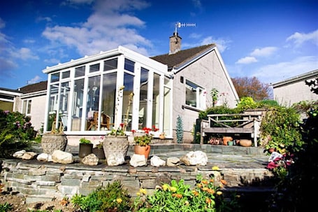 A house with a large glass conservatory, stone steps, and potted plants.