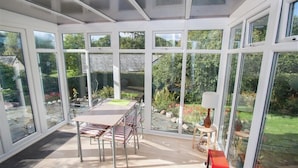 Un invernadero con mesa y sillas, amplias puertas de vidrio y vistas a un jardín.