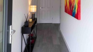 Un couloir avec une porte, une console sur laquelle est posée une lampe, et un tableau abstrait aux couleurs vives accroché au mur.