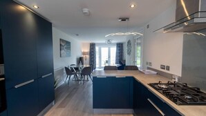 Une cuisine moderne dotée d’un îlot central, de meubles de rangement aux couleurs sombres et d’une cuisinière à gaz.
