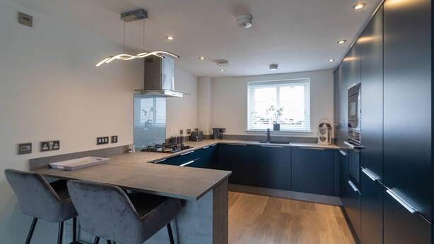Une cuisine moderne avec des meubles de couleur sombre, un plan de travail en bois et une cuisinière intégrée.