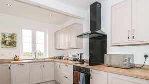 Una cocina moderna con armarios blancos, una campana extractora negra, horno empotrado, tostadora y una ventana que proporciona luz natural.