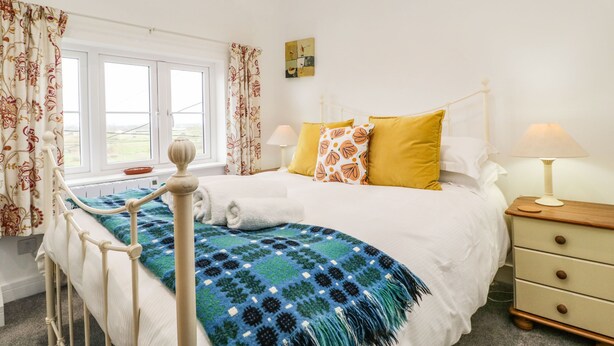 Un dormitorio con cama, mesita de noche, lámpara y ventana con cortinas.