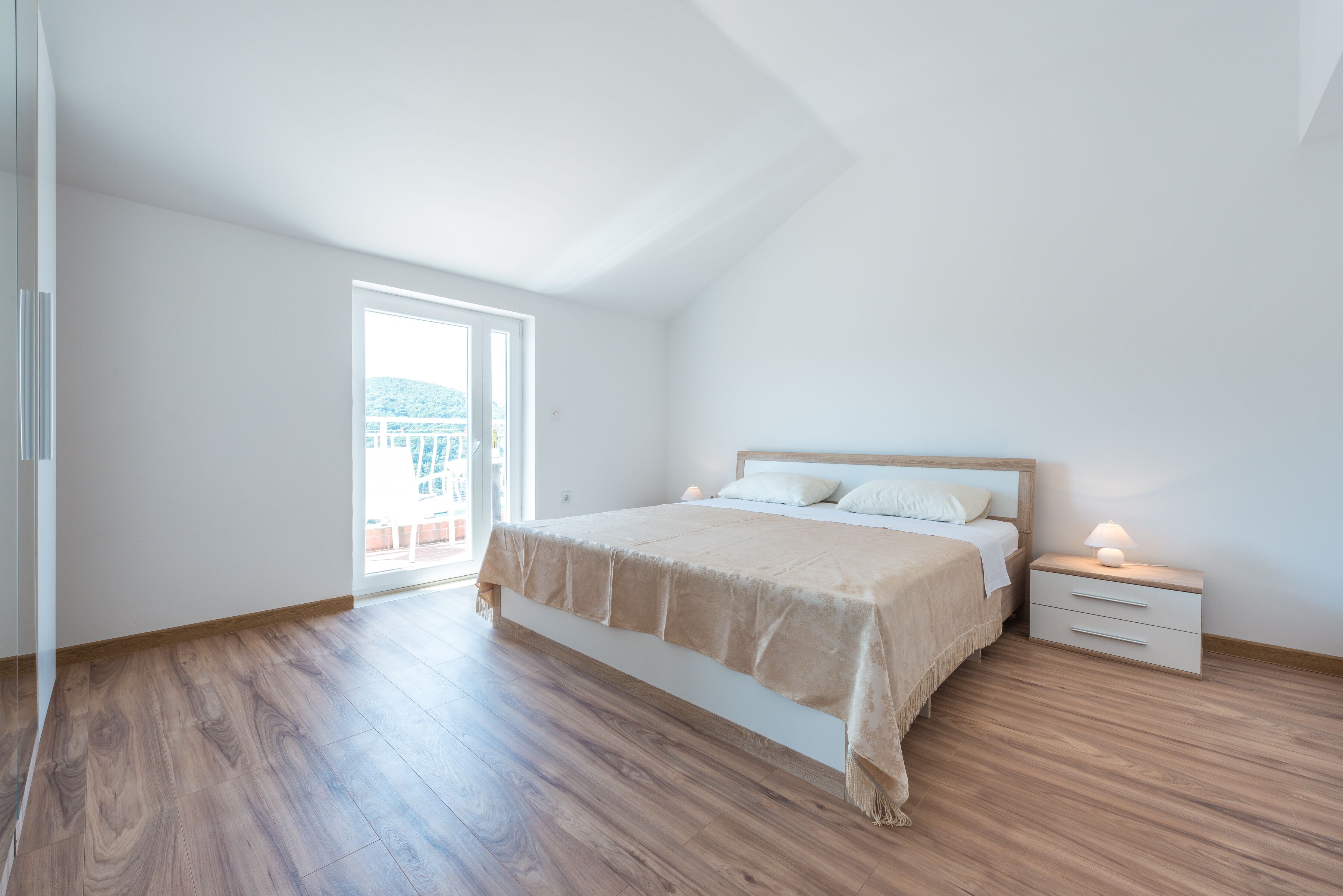 A bedroom with a large bed, a nightstand, a window, and a view of a building outside.
