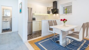 Een moderne keuken met witte kastjes, een roestvrijstalen koelkast en een magnetron. Er is een eethoek met een witte tafel en twee stoelen.