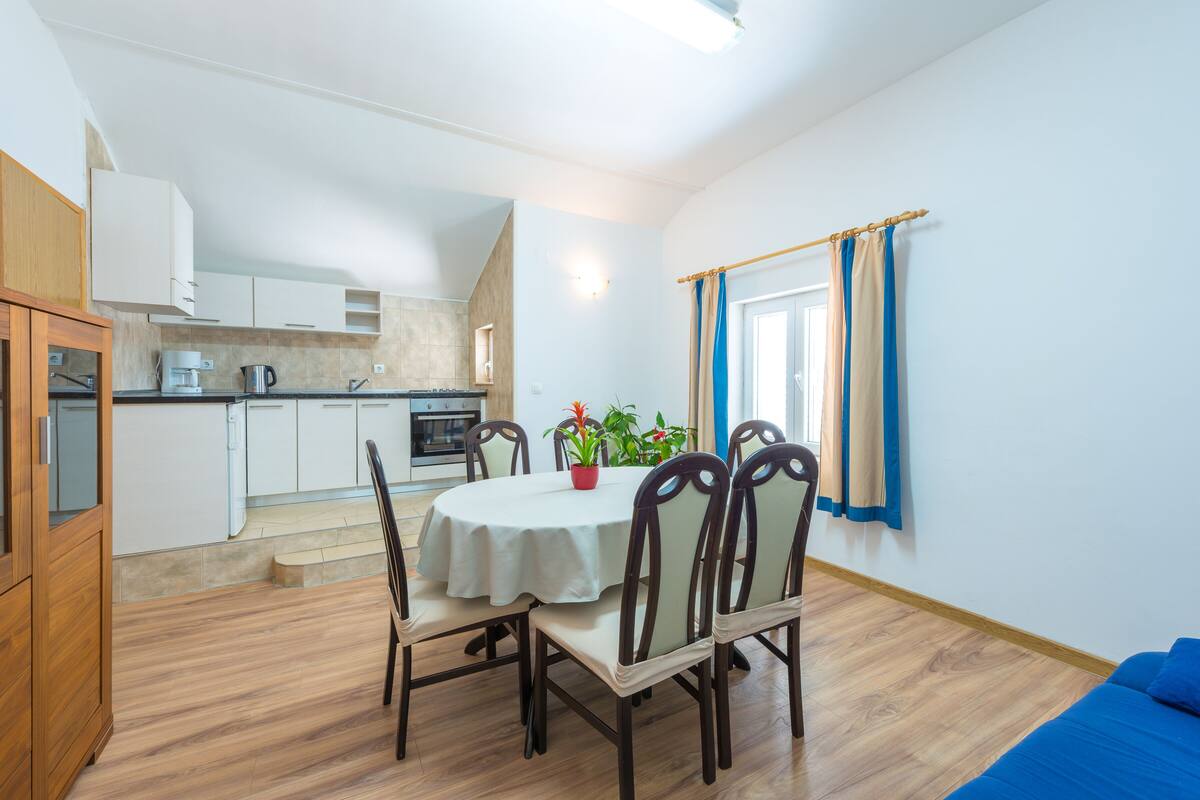 Eine moderne Küche mit weißen Schränken, einem Esstisch mit Stühlen und einem blauen Sofa in einem hellen Raum mit Holzboden.