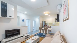 Een moderne woonkamer met een flatscreen televisie, een bank en een eethoek met stoelen en een tafel.
