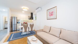 Een moderne woonkamer met een beige bank, een witte salontafel en een eethoek met een tafel en stoelen.