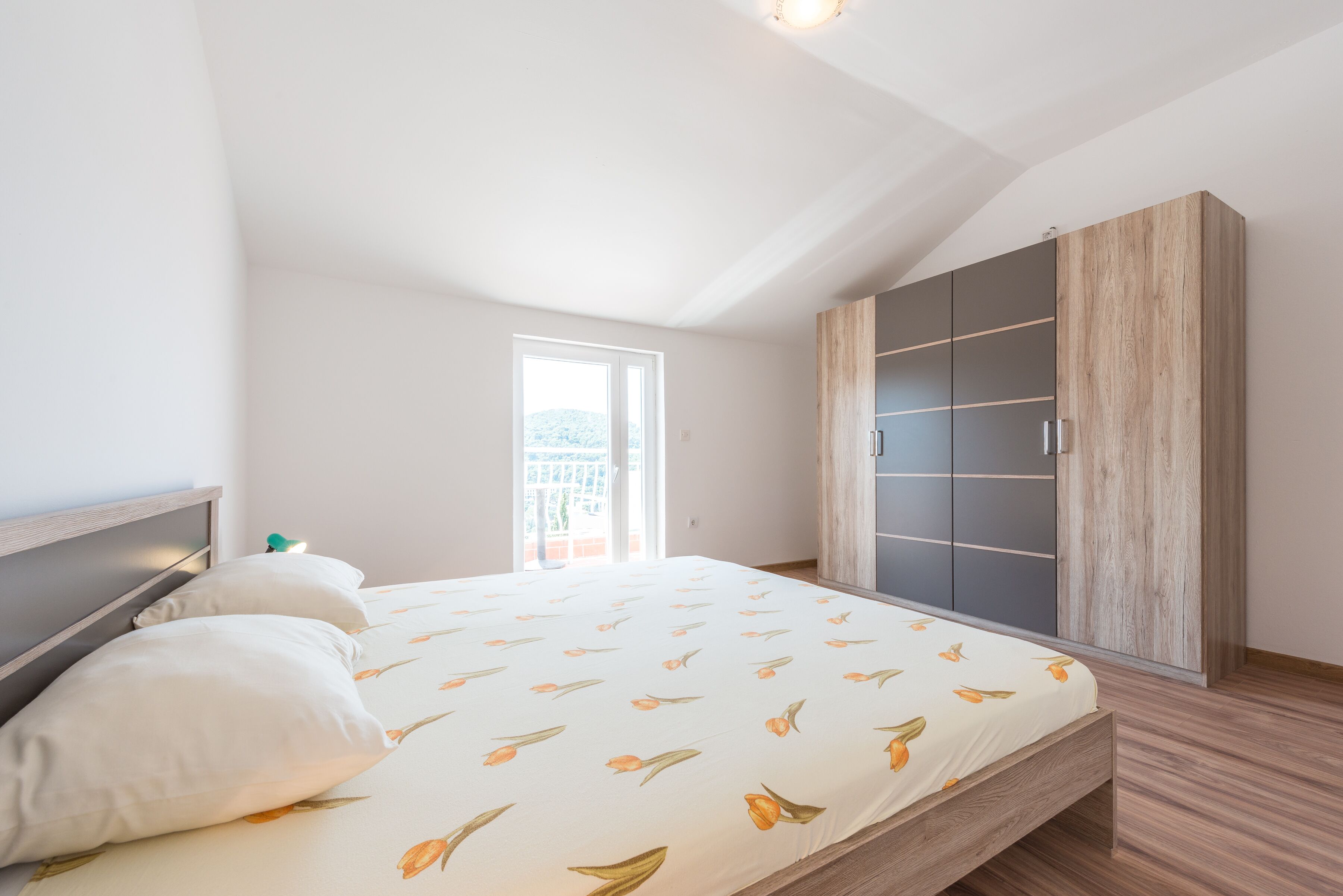 A bedroom with a bed, a wardrobe, and a balcony.