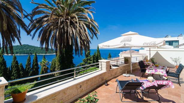 Eine Terrasse mit Sitzgelegenheit im Freien, einem Coca-Cola Sonnenschirm und Blick auf das Meer.