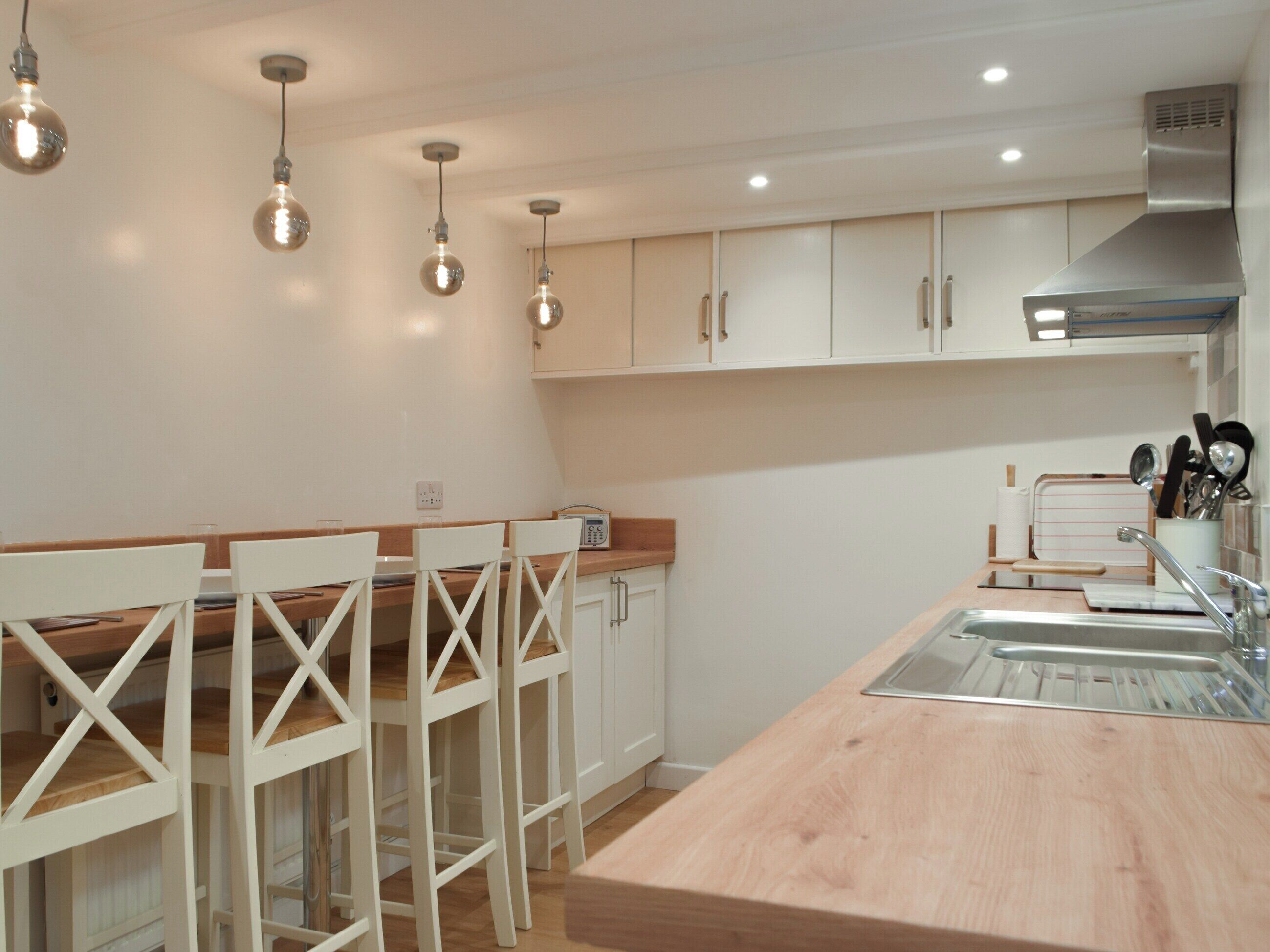 A modern kitchen with white cabinets, a wooden countertop, and hanging light fixtures.