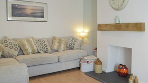 Ein Wohnzimmer mit einer Couch, Kissen, einer Lampe, einer Uhr, einem Kamin und einem gerahmten Bild an der Wand.