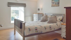 Ein Schlafzimmer mit Bett, Nachttisch, Lampe und einem Fenster mit Blick auf Grünflächen.