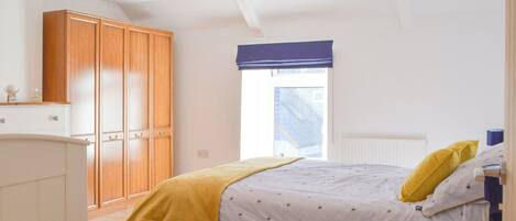 A bedroom with a bed, wooden wardrobe, and a window with a blue blind.