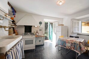 A kitchen with a stove, oven, and sink, a dining table with a tablecloth, and a door leading outside. - Apartment "Bilocale Victor" near the beach (Bonassola SP)