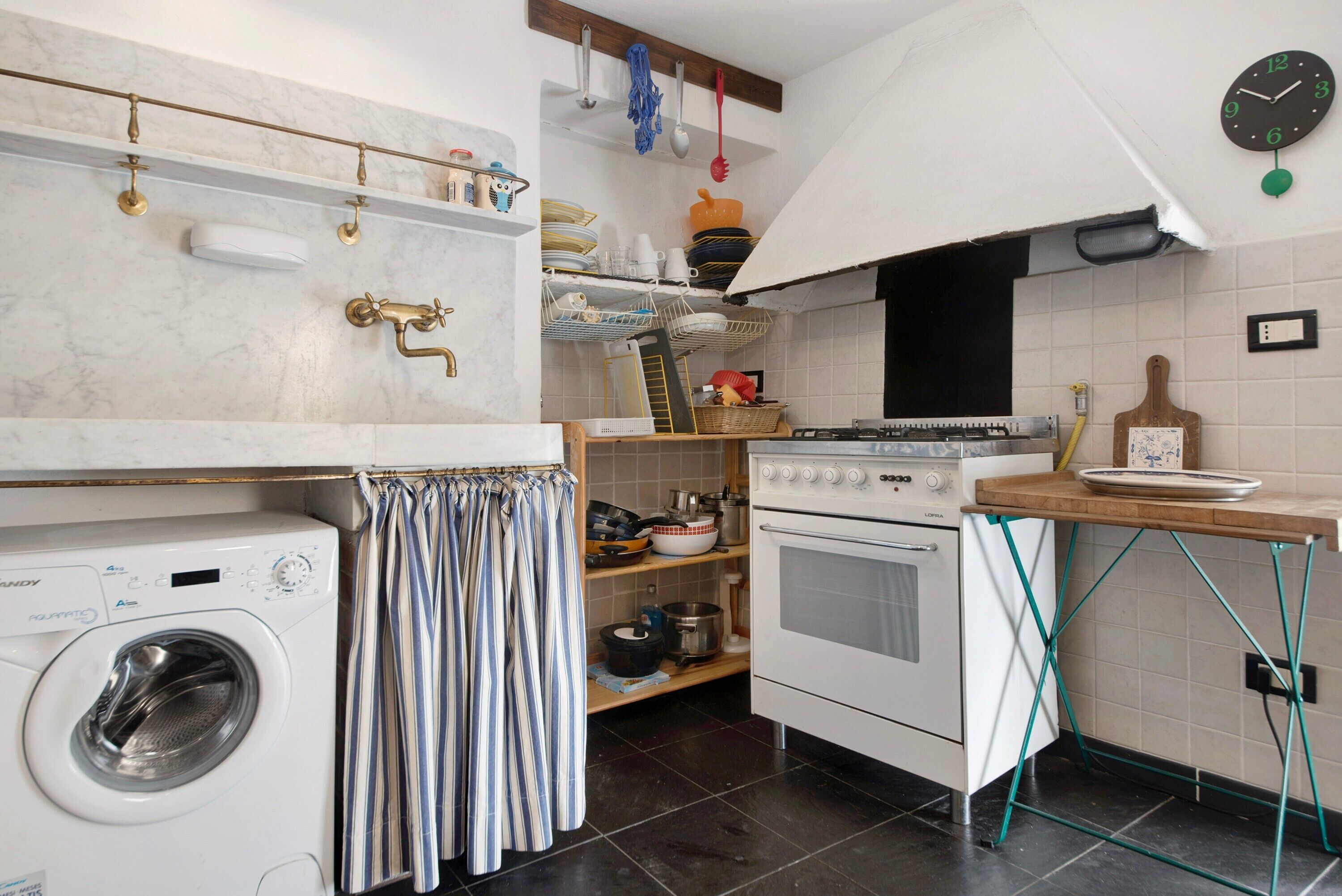 Una cucina compatta con lavatrice, fornello e ripiani con stoviglie e utensili.